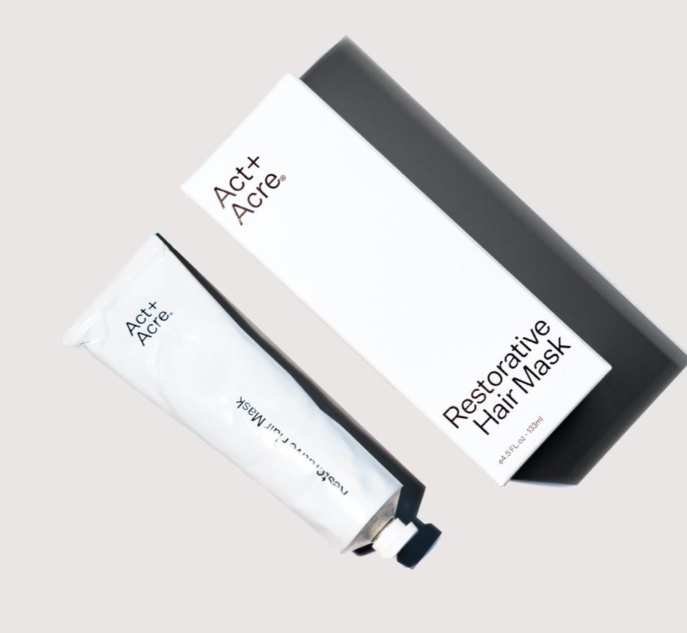 A tube and a box of Act+Acre Restorative Hair Mask packaging against a plain light gray background.