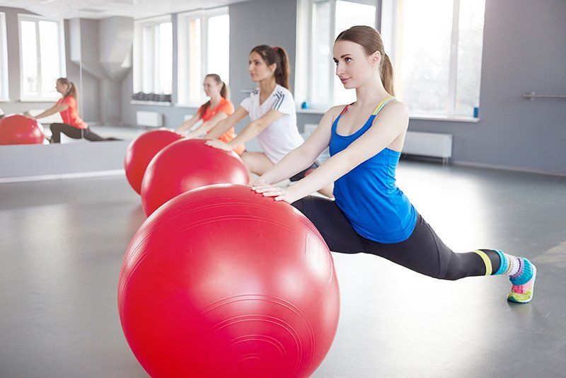 Un grupo de mujeres están sentadas sobre pelotas de ejercicio rojas en un gimnasio.