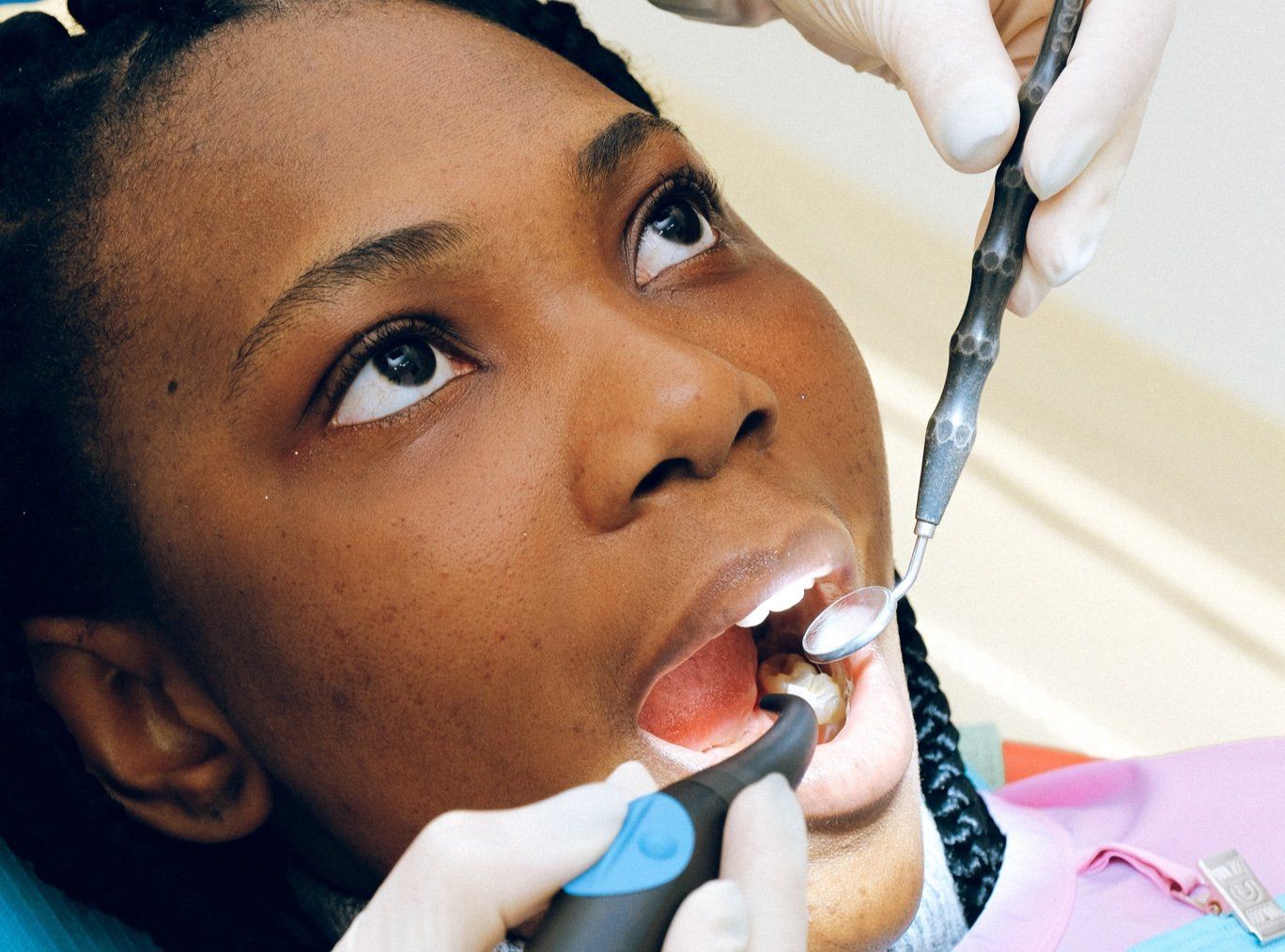 Person at dentist, mouth open, receiving dental cleaning. Dentist holding tools.