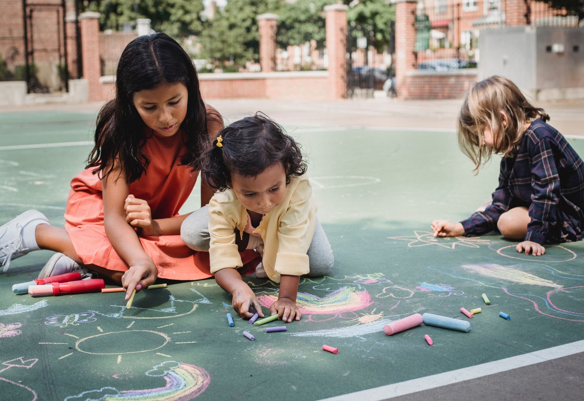 Drie kinderen tekenen met krijt op een groen oppervlak buiten.