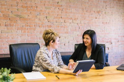 Two women are sitting at a table looking at a tablet.