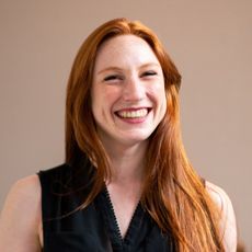 A woman with long red hair is smiling and wearing a black shirt