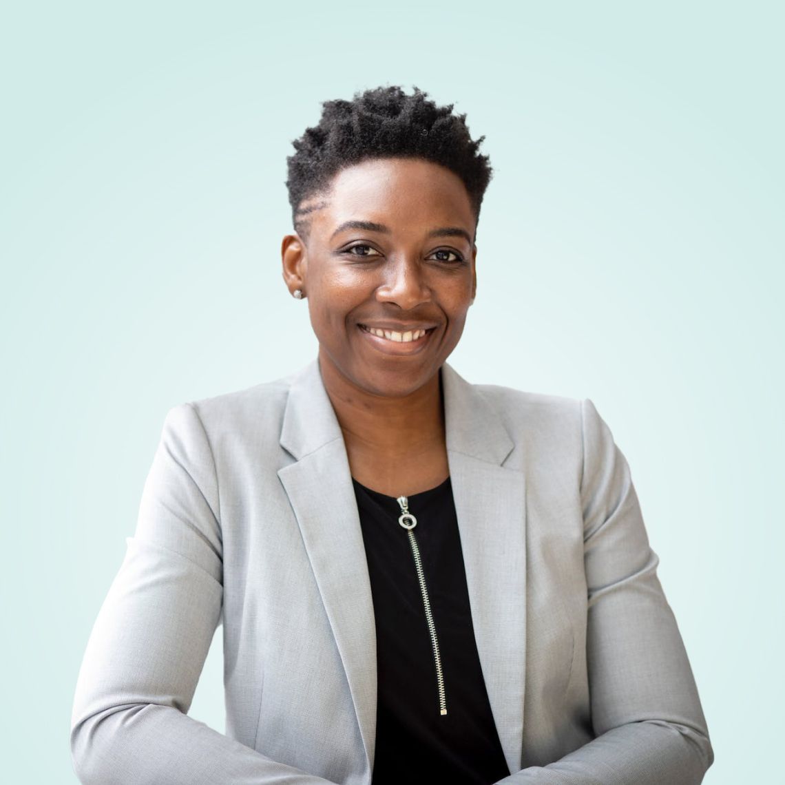 Smiling person in a light gray blazer seated against a pale blue background