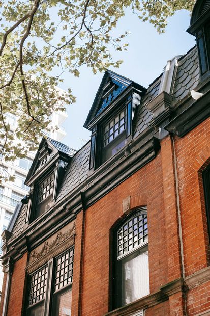 Brick building with black roof dormers and arched windows, seen from below against trees and sky
