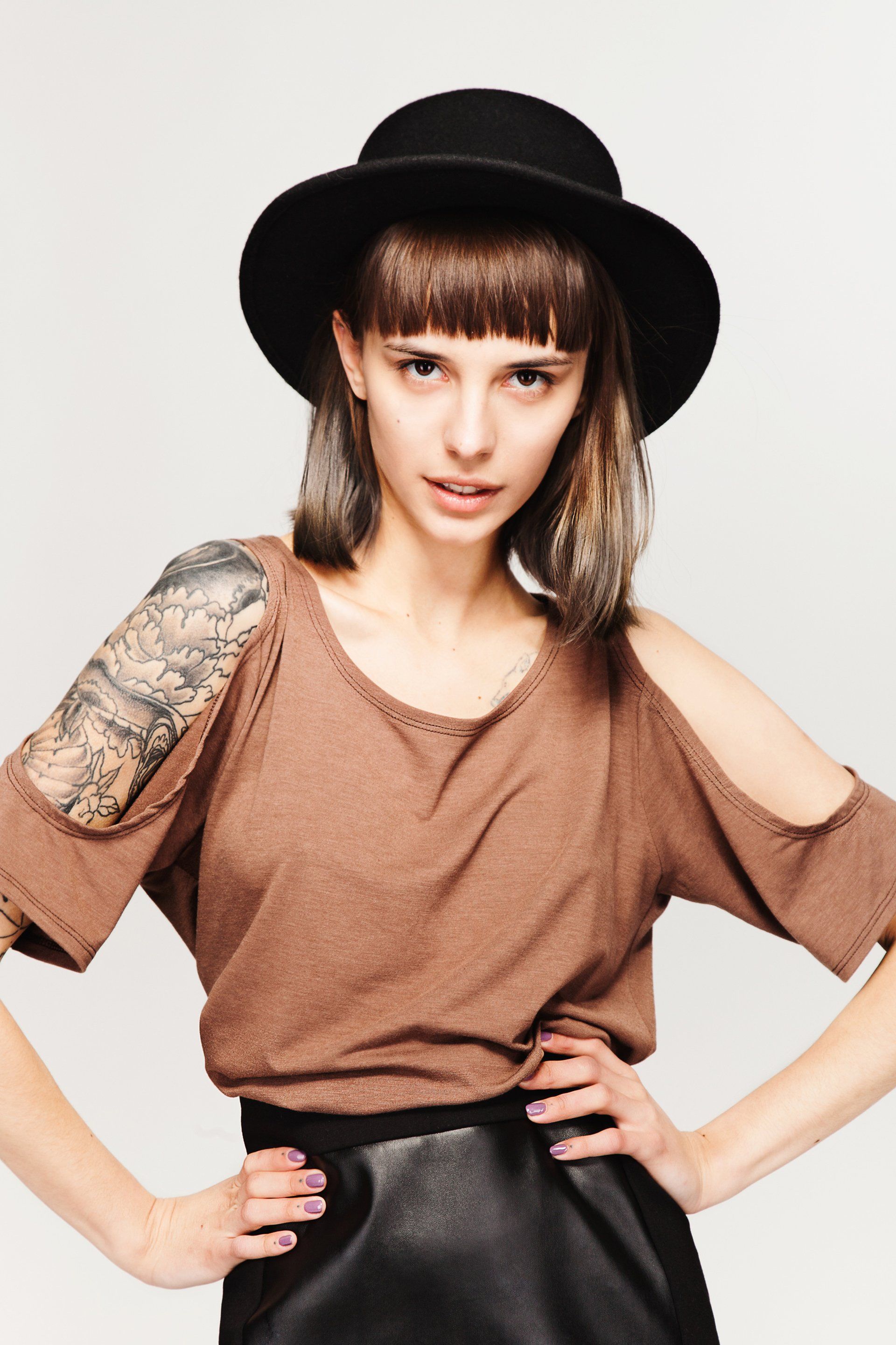 A woman wearing a hat and a brown shirt has a tattoo on her arm