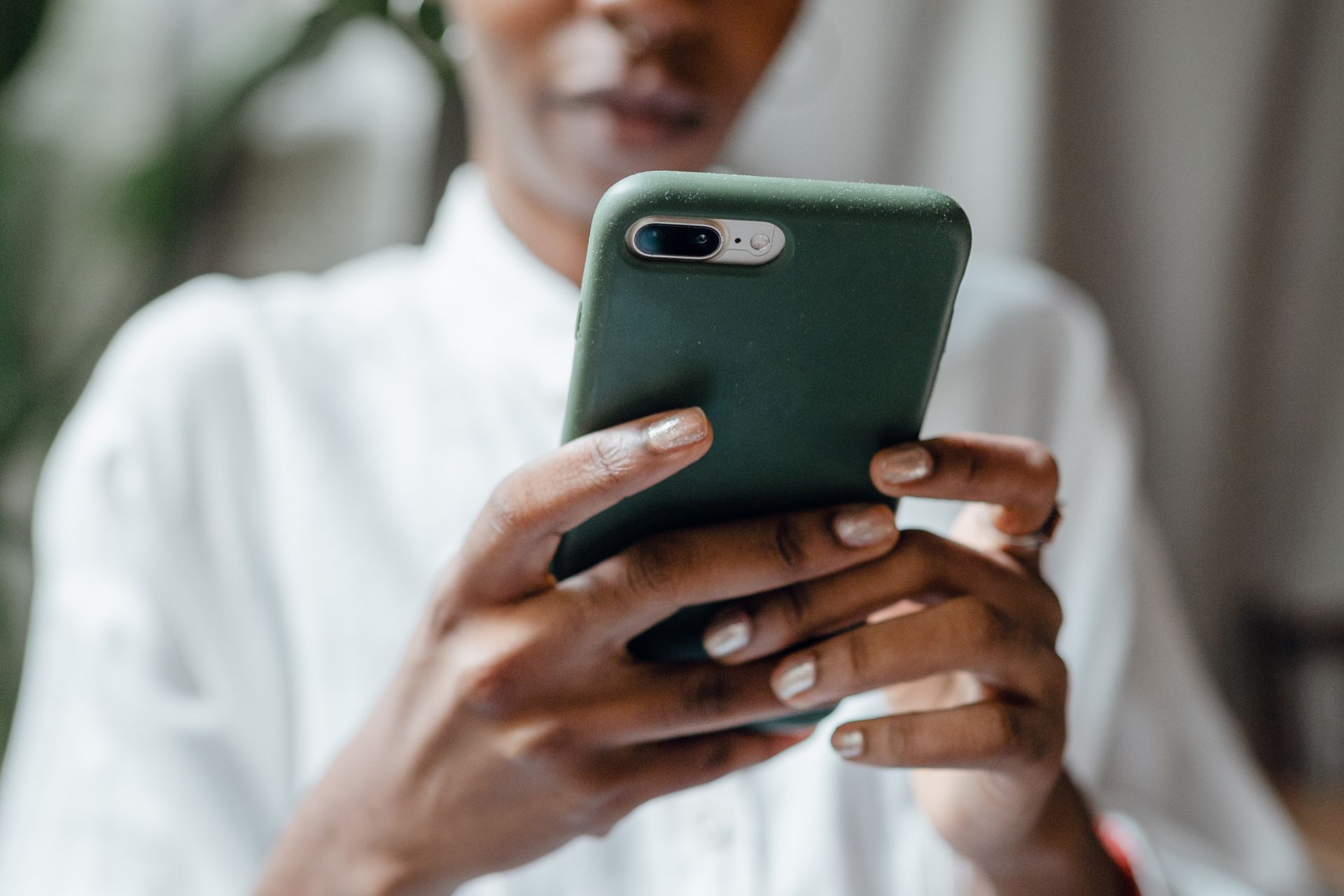 Person holding a green smartphone, typing with their thumbs, in a white shirt.