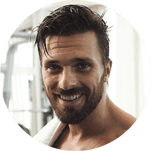 A man with a beard is smiling with a towel around his neck.