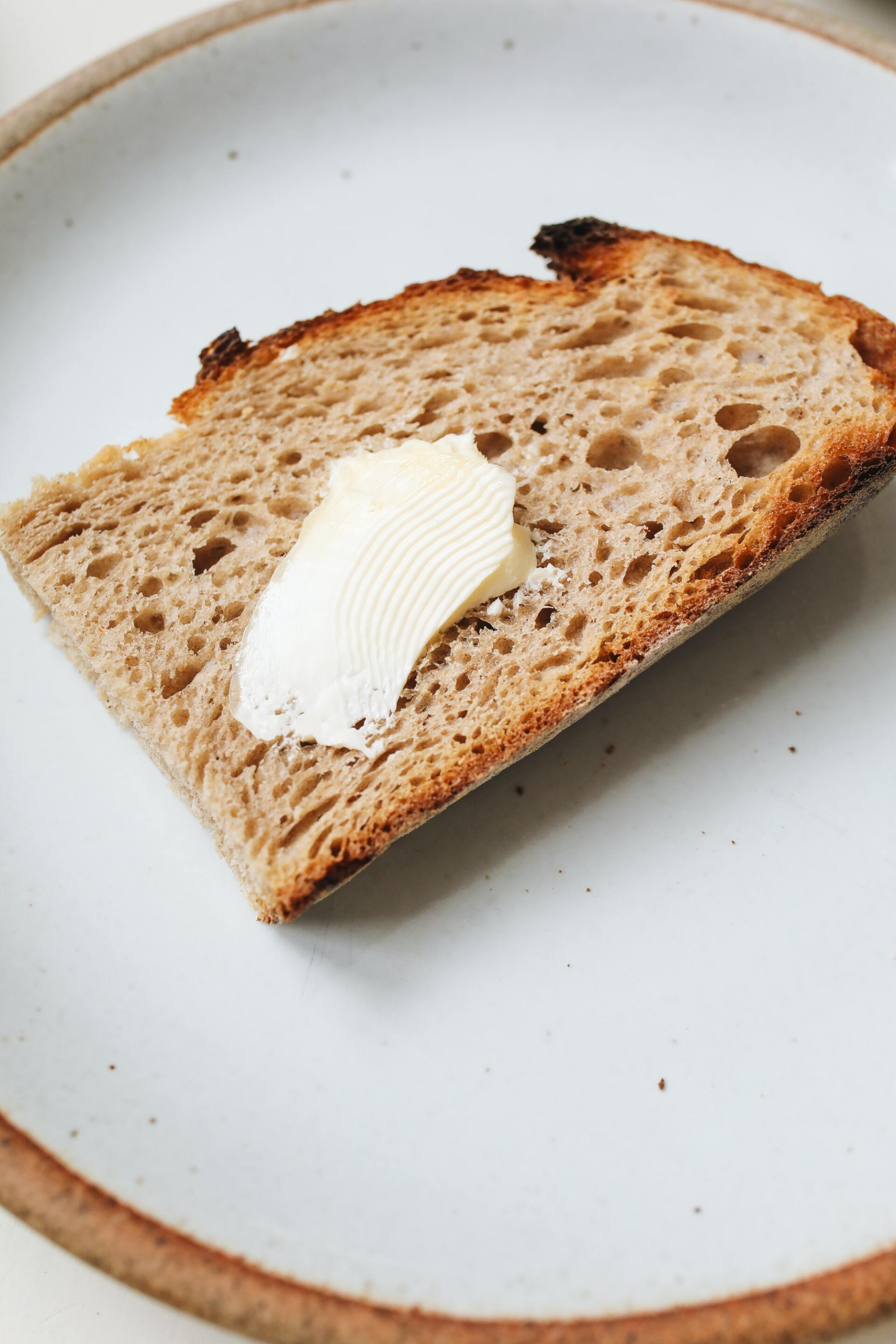 A slice of bread with butter on it on a white plate.