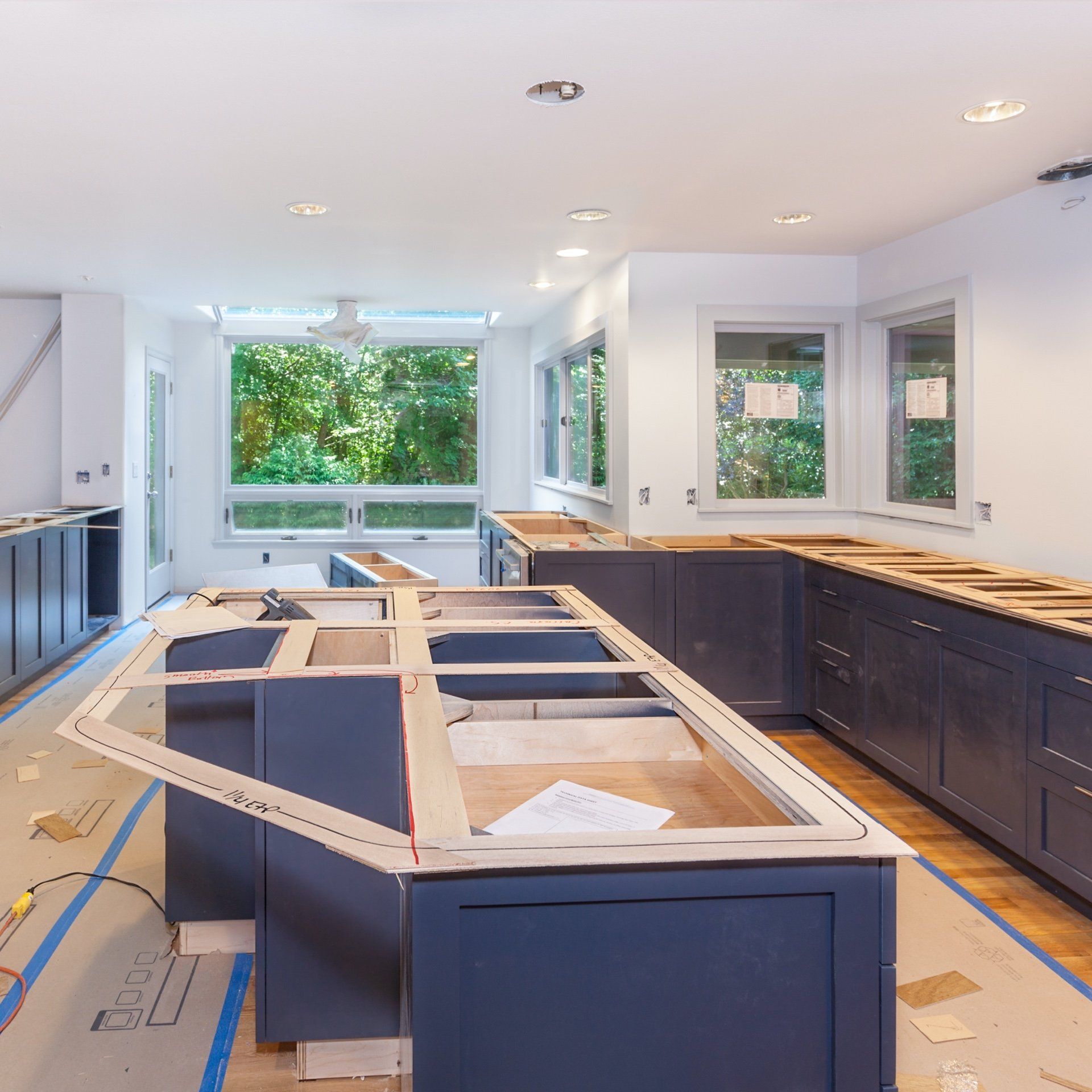 Kitchen renovation in progress. Navy blue cabinets installed, island frame visible, windows in background.