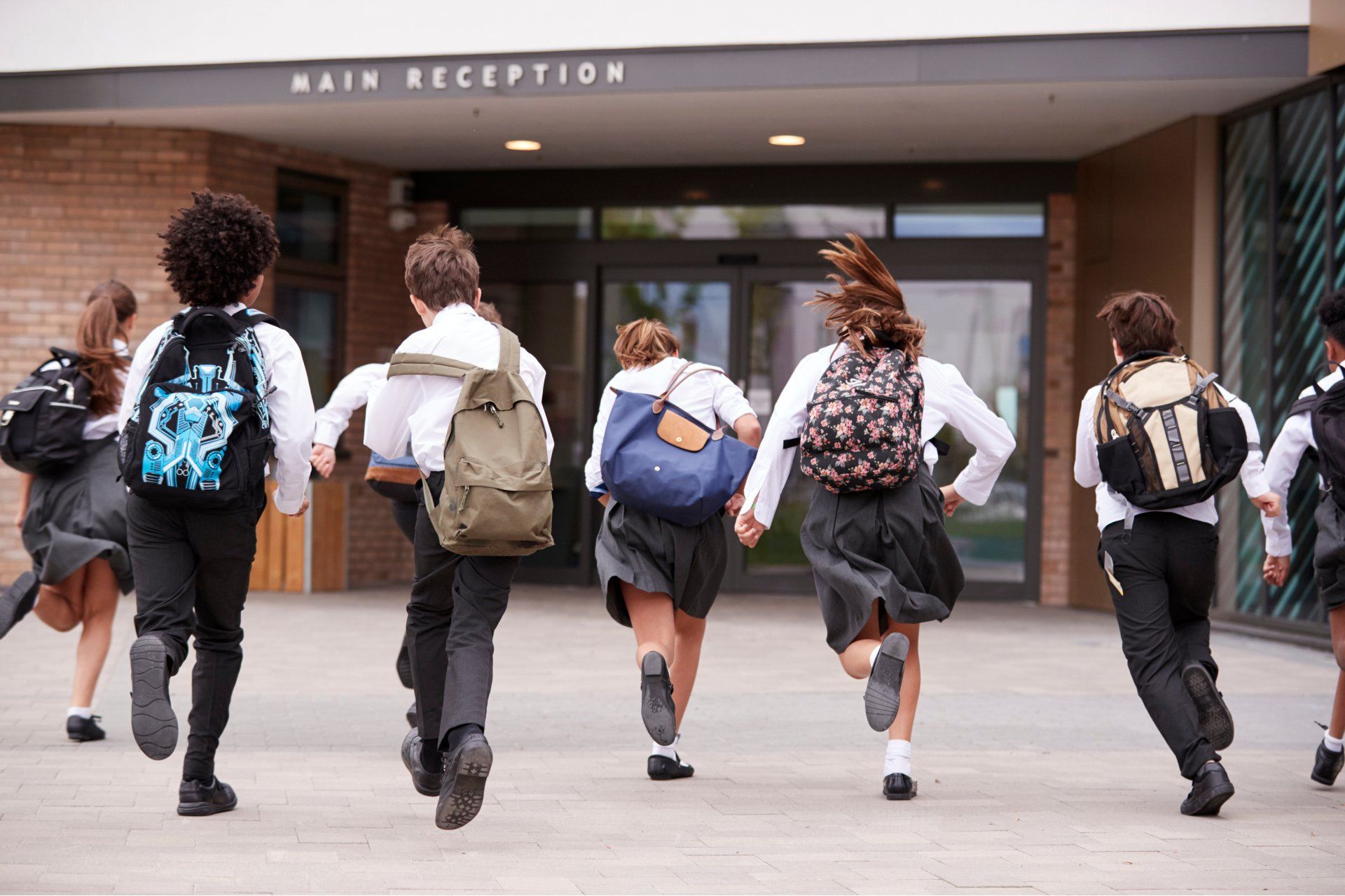 Students in school uniforms running towards a building entrance with
