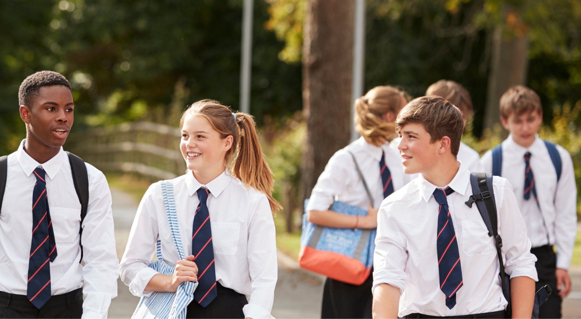 Students in uniform walking outdoors; smiling, carrying backpacks, some looking at each other.