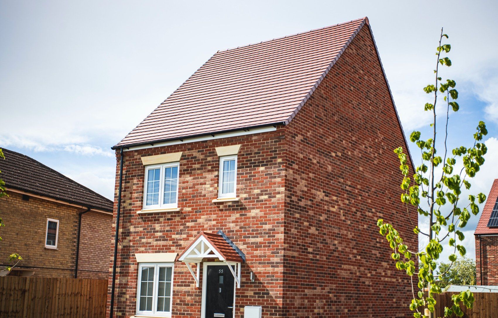 A red brick house with a white door and a red roof in a residential area.