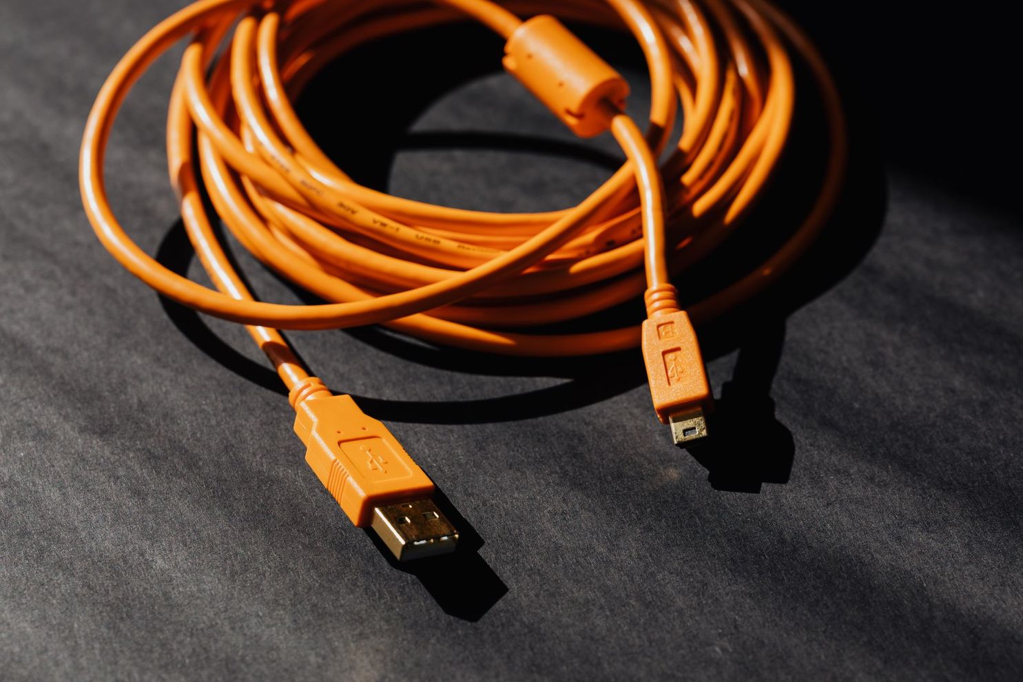 Orange USB cable coiled on a dark surface, with one USB-A end and one smaller connector visible