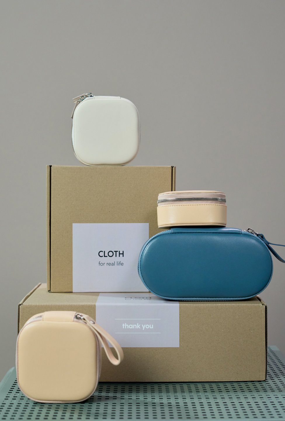 Arrangement of cosmetic bags and boxes. Beige, white and blue bags stacked with brown boxes against a gray background.