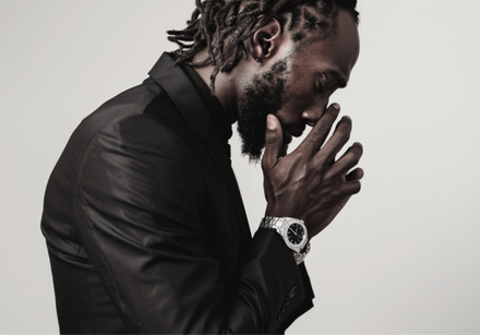 A man with dreadlocks is wearing a black suit and a watch.