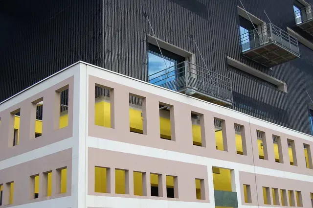 An exterior view of a building with a beige facade featuring many rectangular windows and a dark, modern upper section.