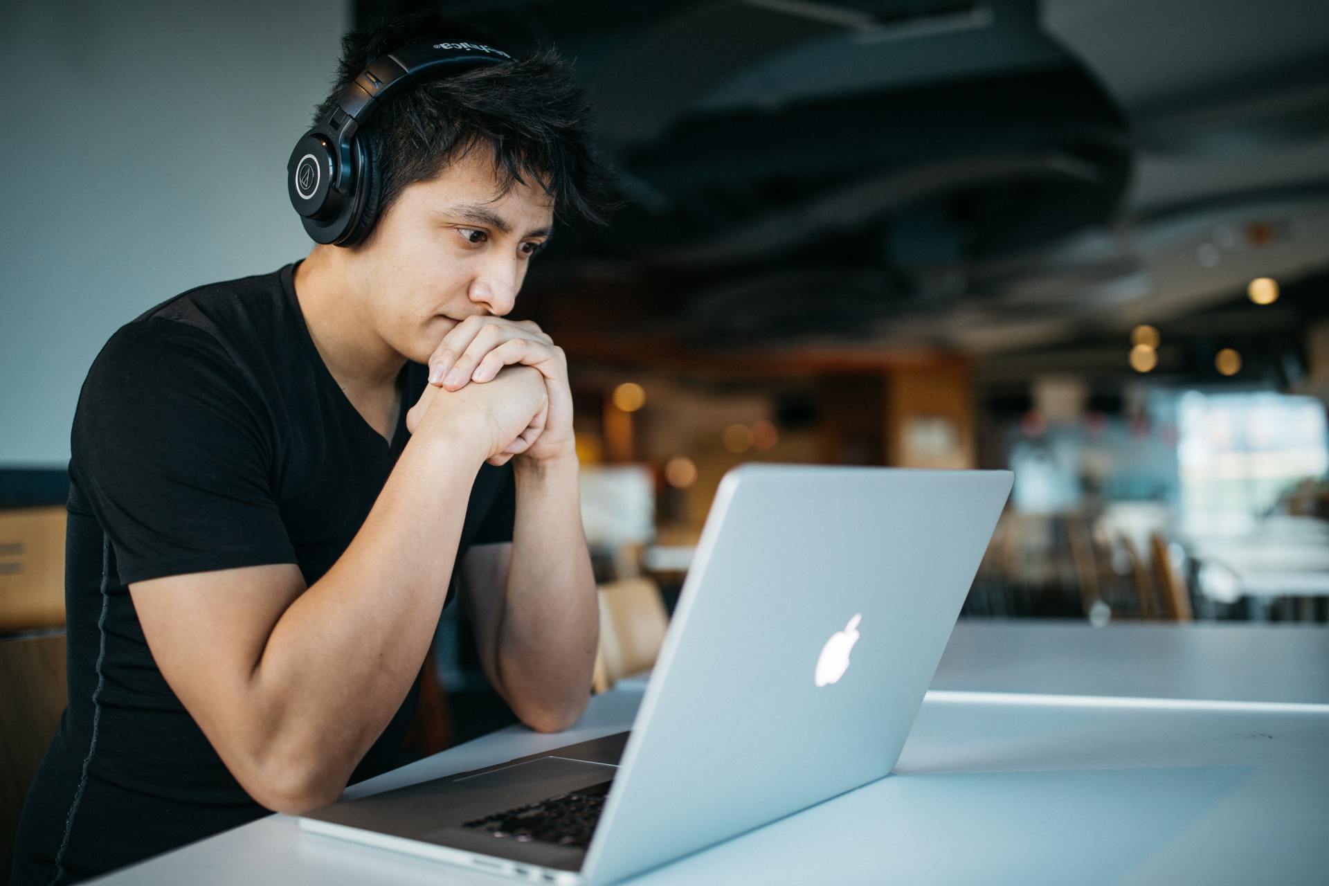 A man wearing headphones is looking at a laptop computer.