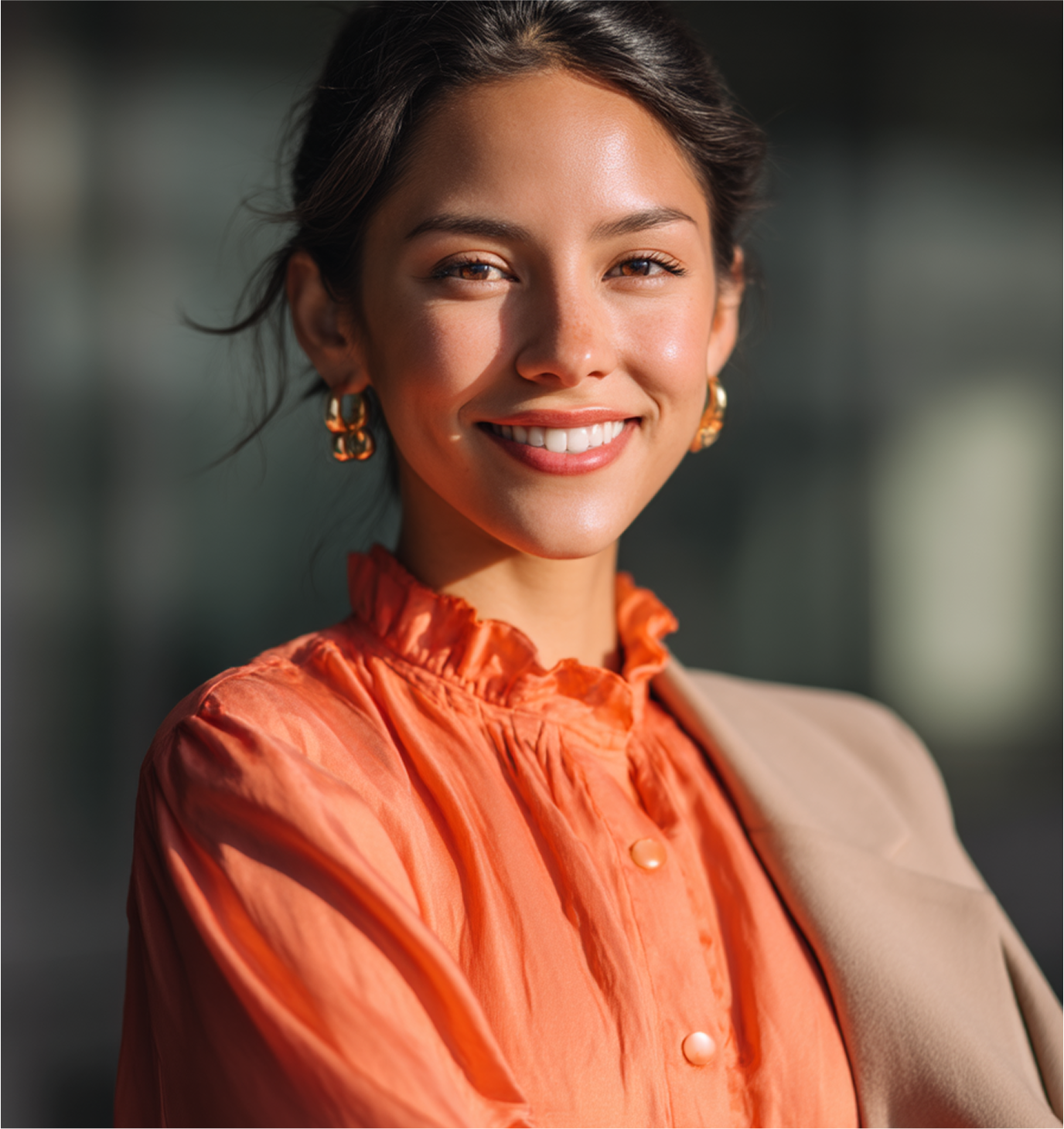 Woman smiling, wearing orange top, gold earrings, beige blazer outdoors.