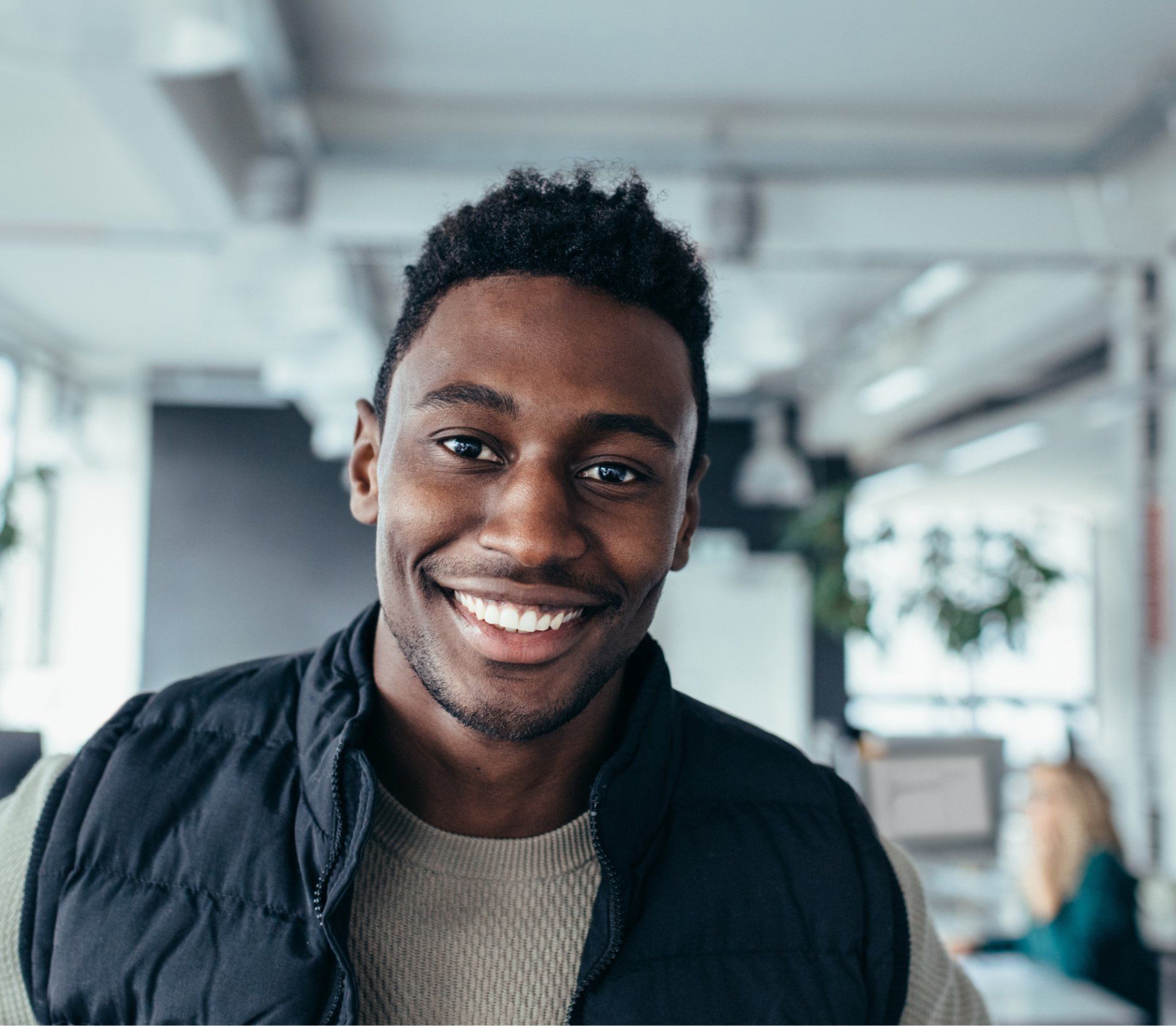 A man wearing a black vest and a sweater is smiling for the camera.