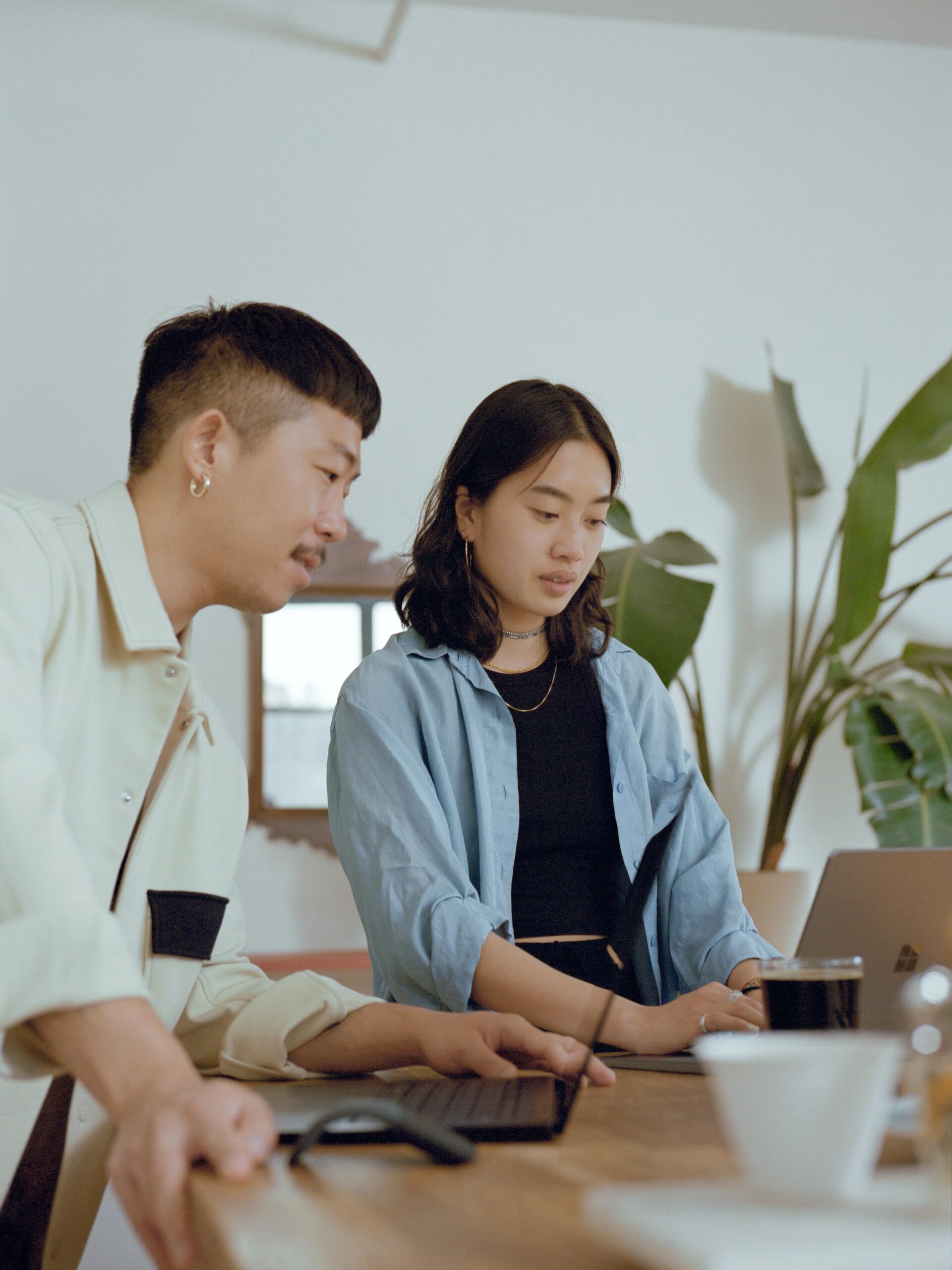 A man and a woman are sitting at a table looking at a laptop.