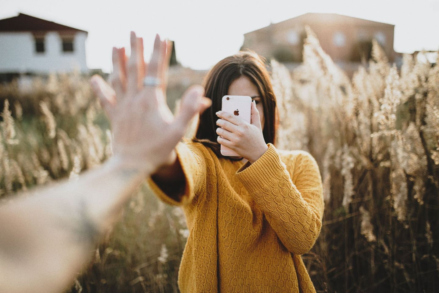 a woman in a yellow sweater covering her face with her hand while holding an apple iphone