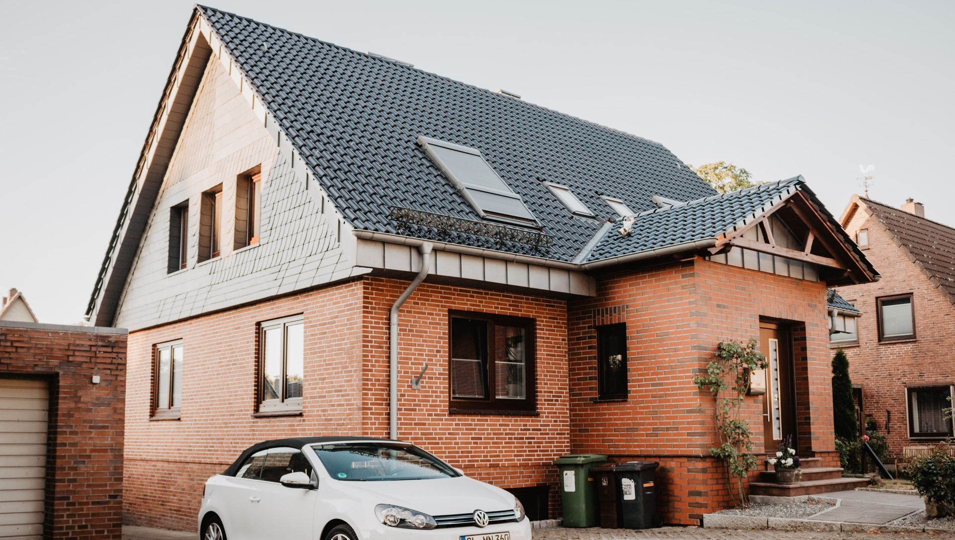 Brick house with gray roof, a white car parked in front.