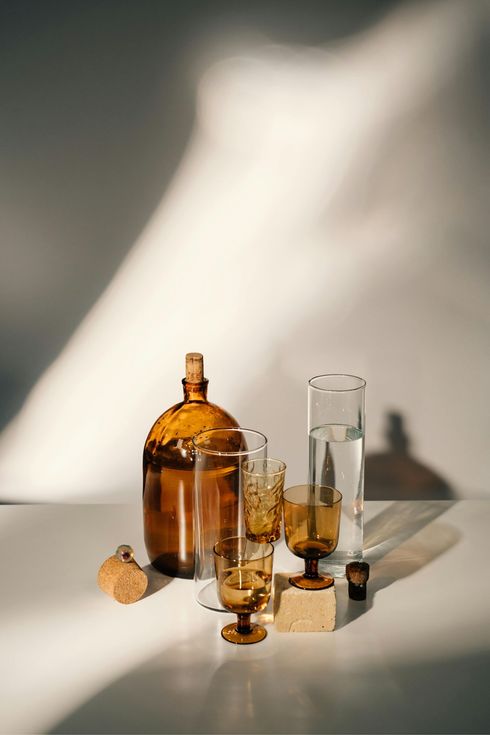 Amber and clear glass bottles on a sunlit table casting long shadows
