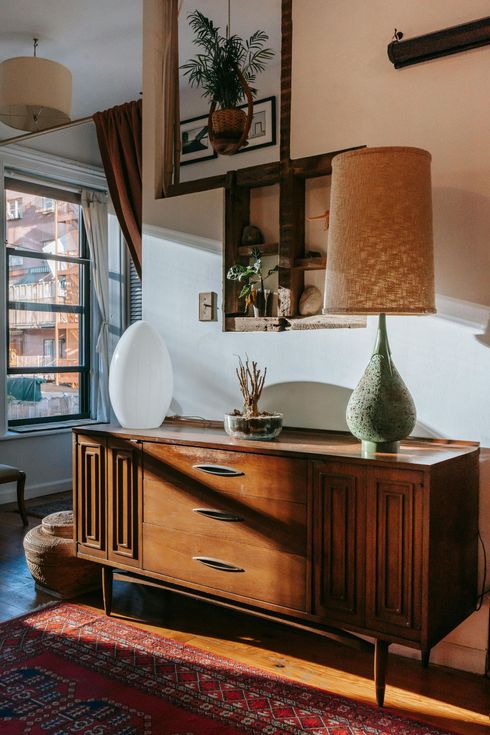 Stylish living room with a wooden sideboard, two table lamps, wall shelves, and a red patterned rug.