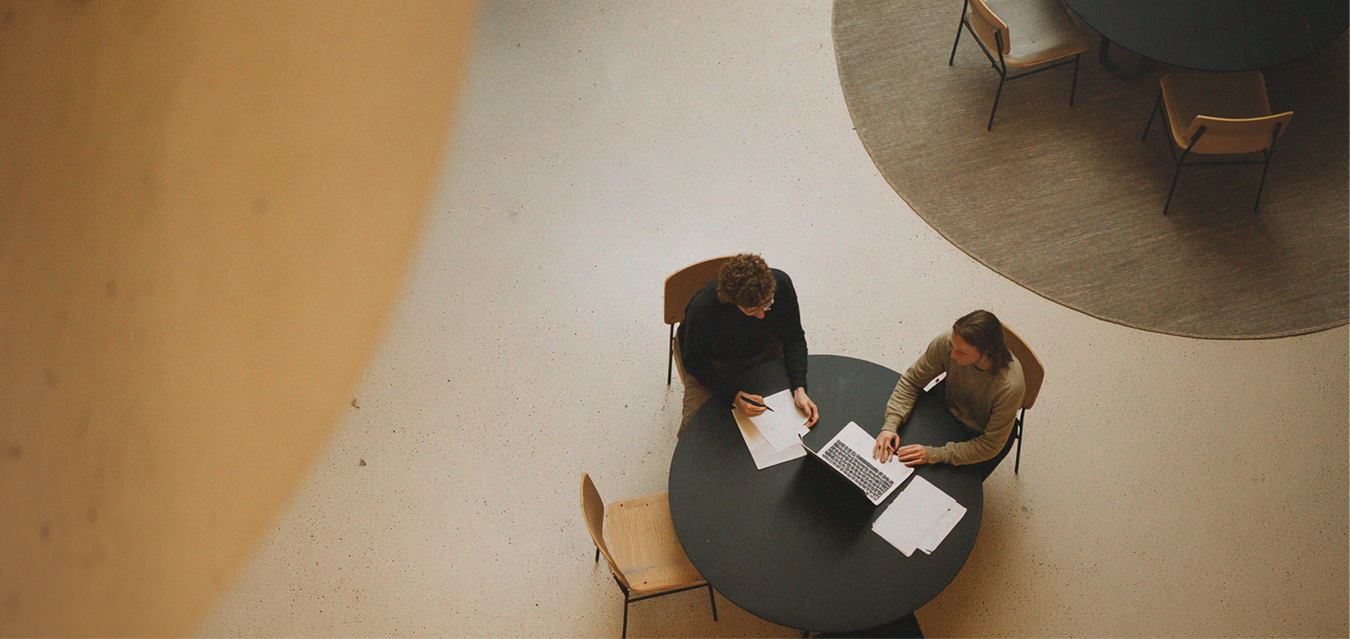 Two people reviewing papers at a round table in a bright indoor lobby