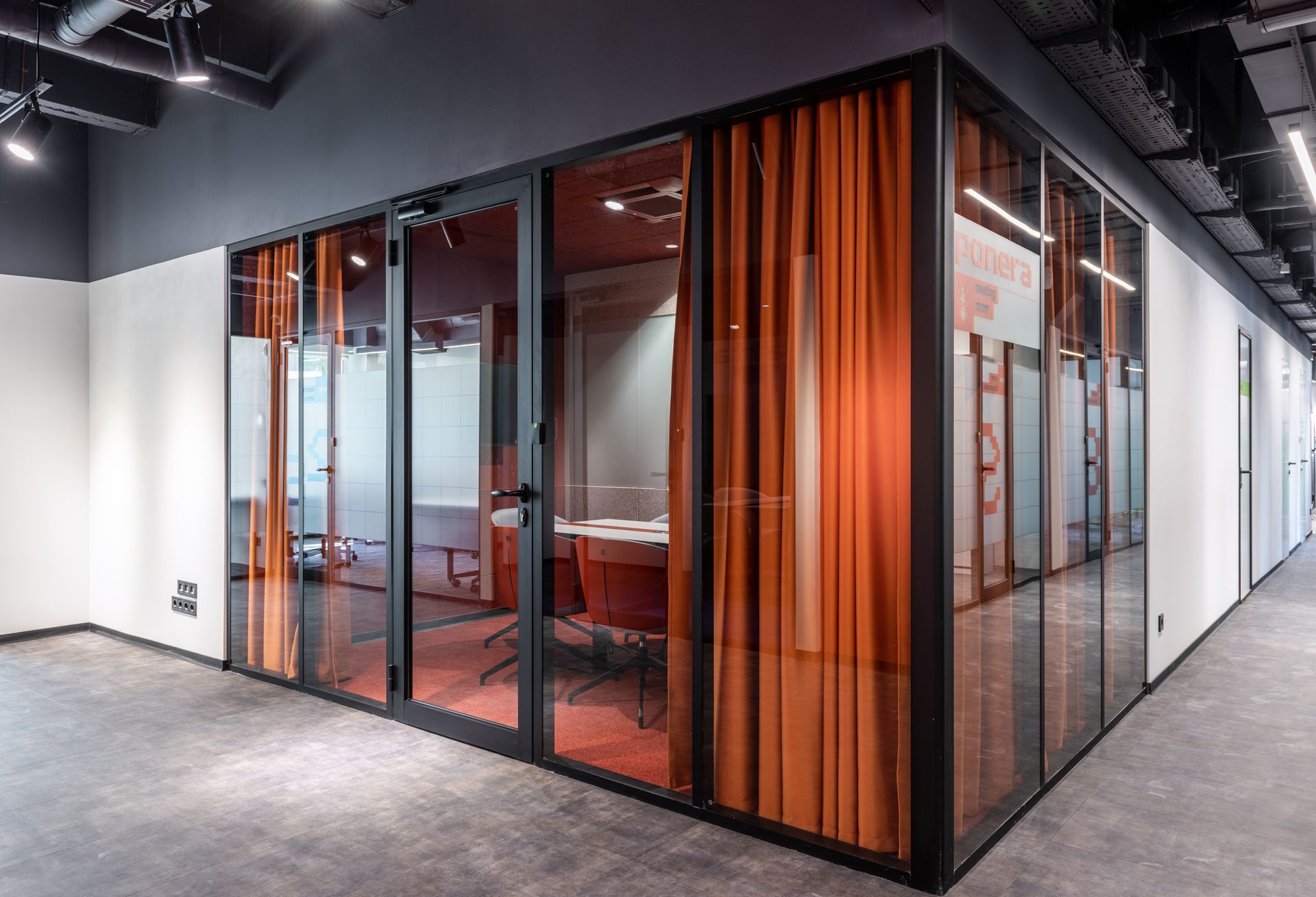 Glass-walled office space with orange curtains. Dark frames and gray carpet.