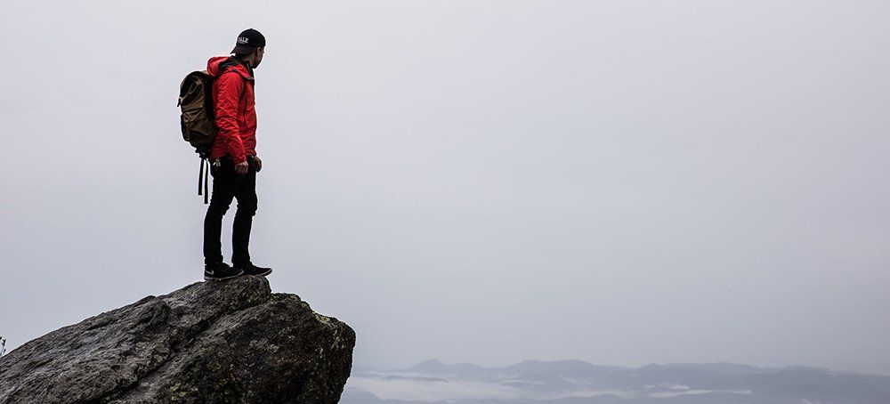 A man with a backpack is standing on top of a rock.