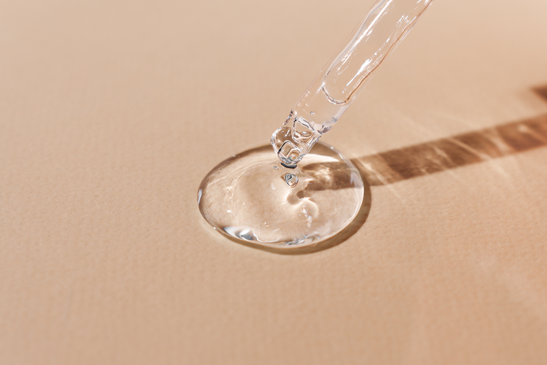 Clear liquid serum being dispensed from dropper onto a tan surface.