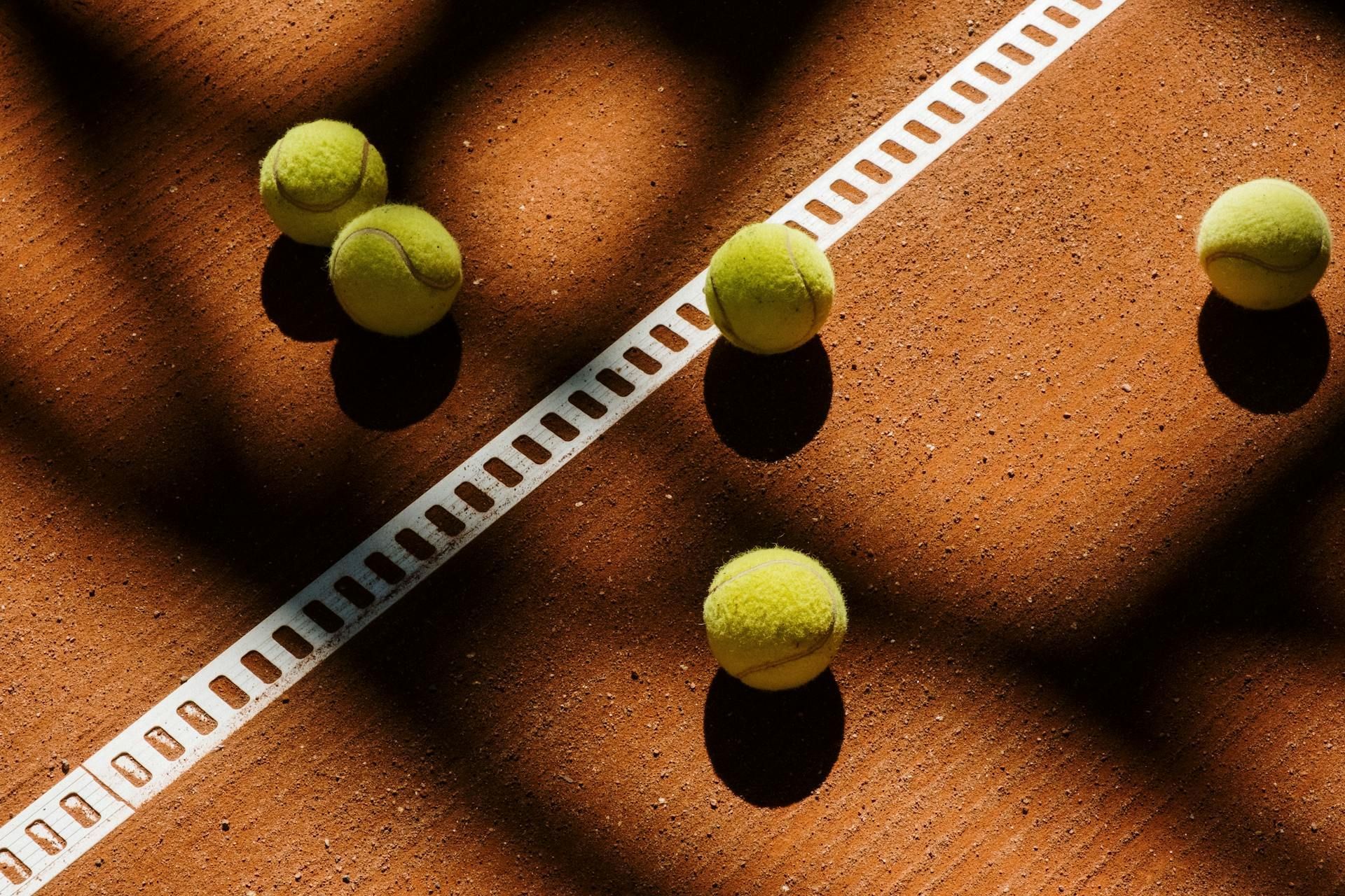Tennis balls on a clay court with a white line.