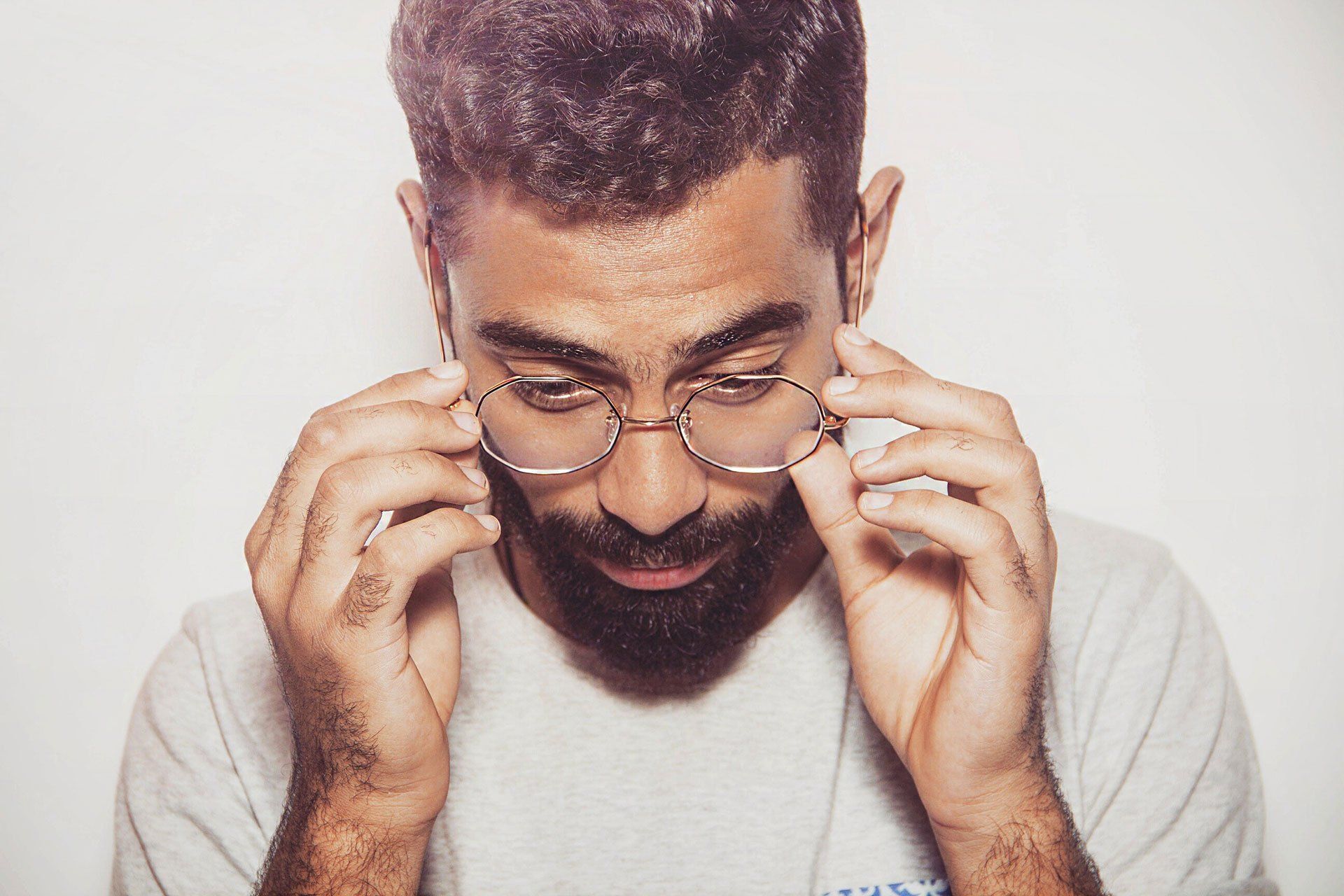 A man with a beard is wearing glasses and looking down.