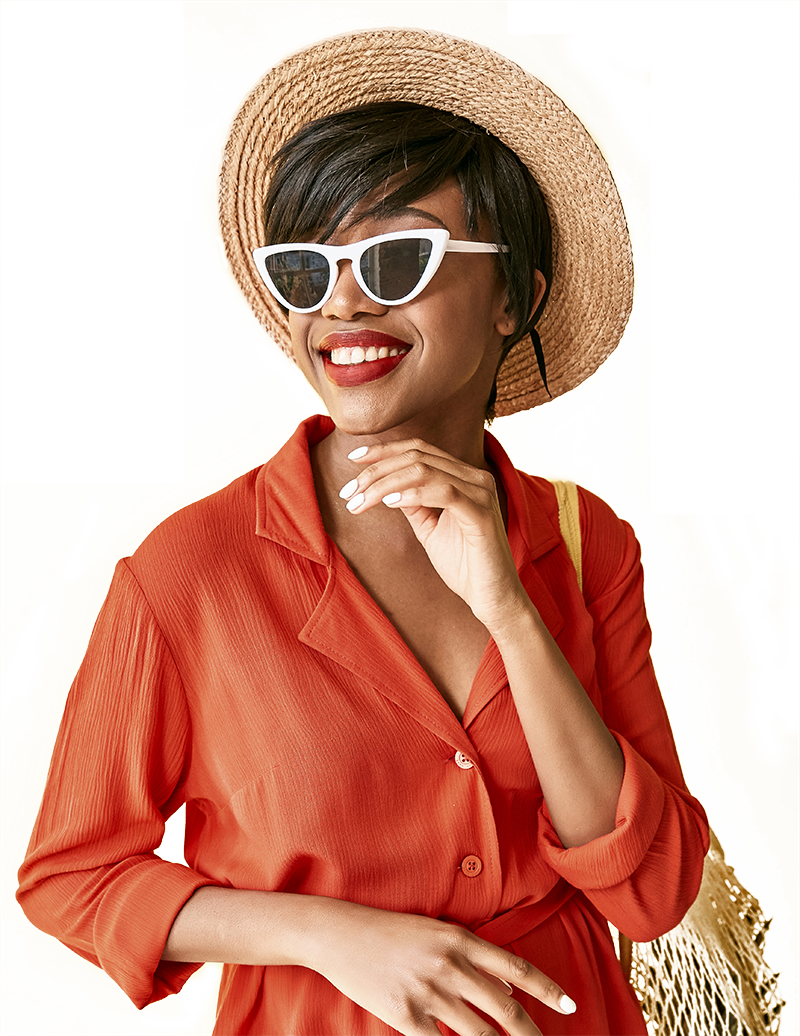 Woman in sunglasses, hat, and orange shirt smiles, with gold bag on shoulder.