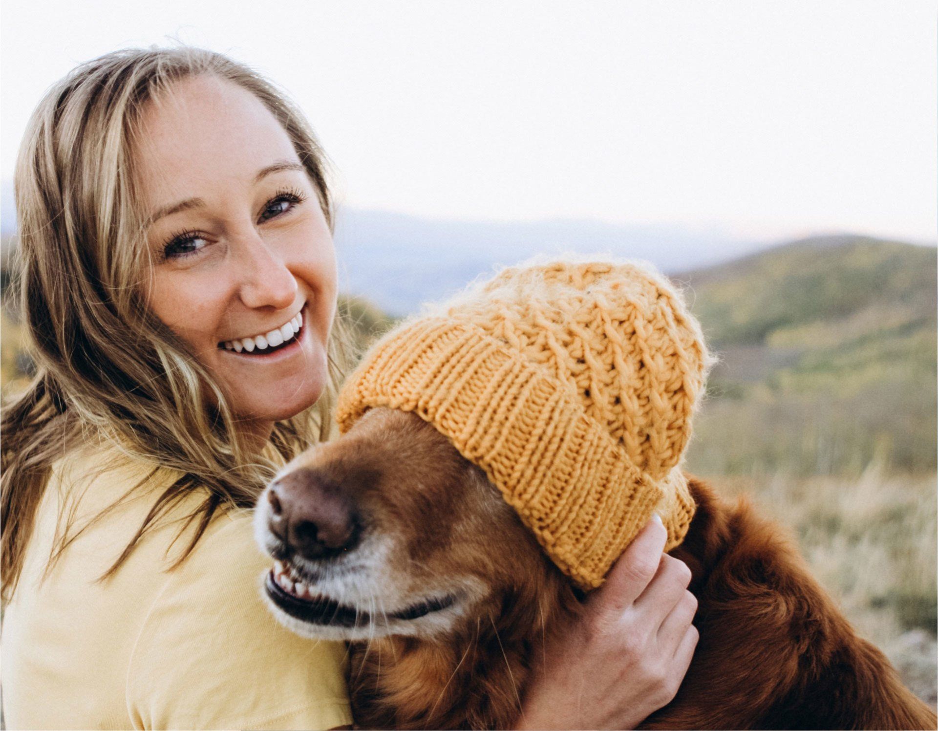 A woman is hugging a dog wearing a yellow hat.