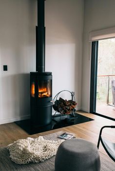 Black wood-burning stove with lit fire in a modern living room, firewood basket nearby, and a rug.