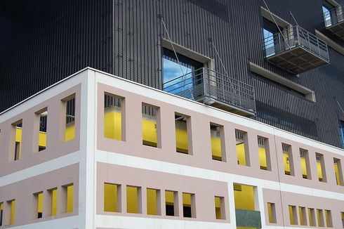 Modern building with a light pink facade and dark gray upper levels. Windows reflect a blue sky.
