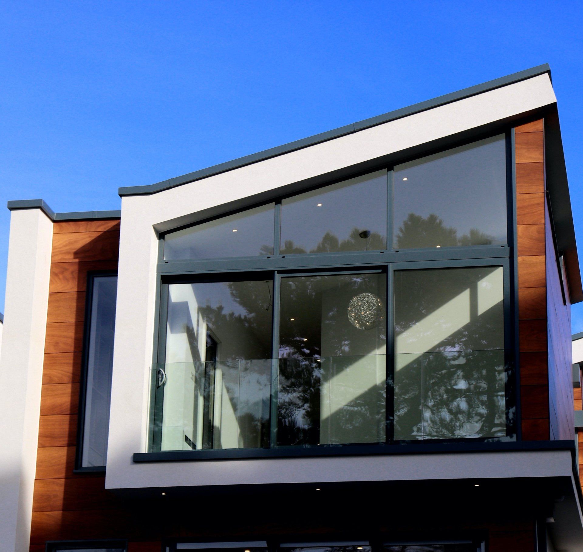 Modern building exterior with large windows, wood paneling, and a bright blue sky.