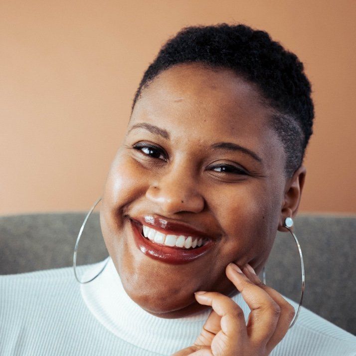 A woman wearing hoop earrings is smiling and touching her face.