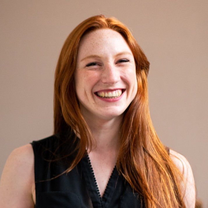A woman with long red hair is smiling and wearing a black shirt