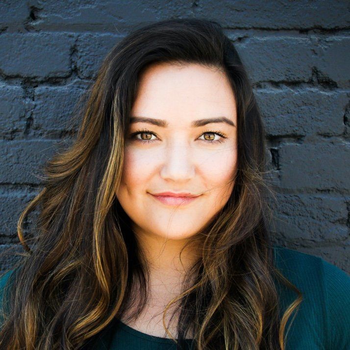 A woman with long hair is smiling in front of a black brick wall.