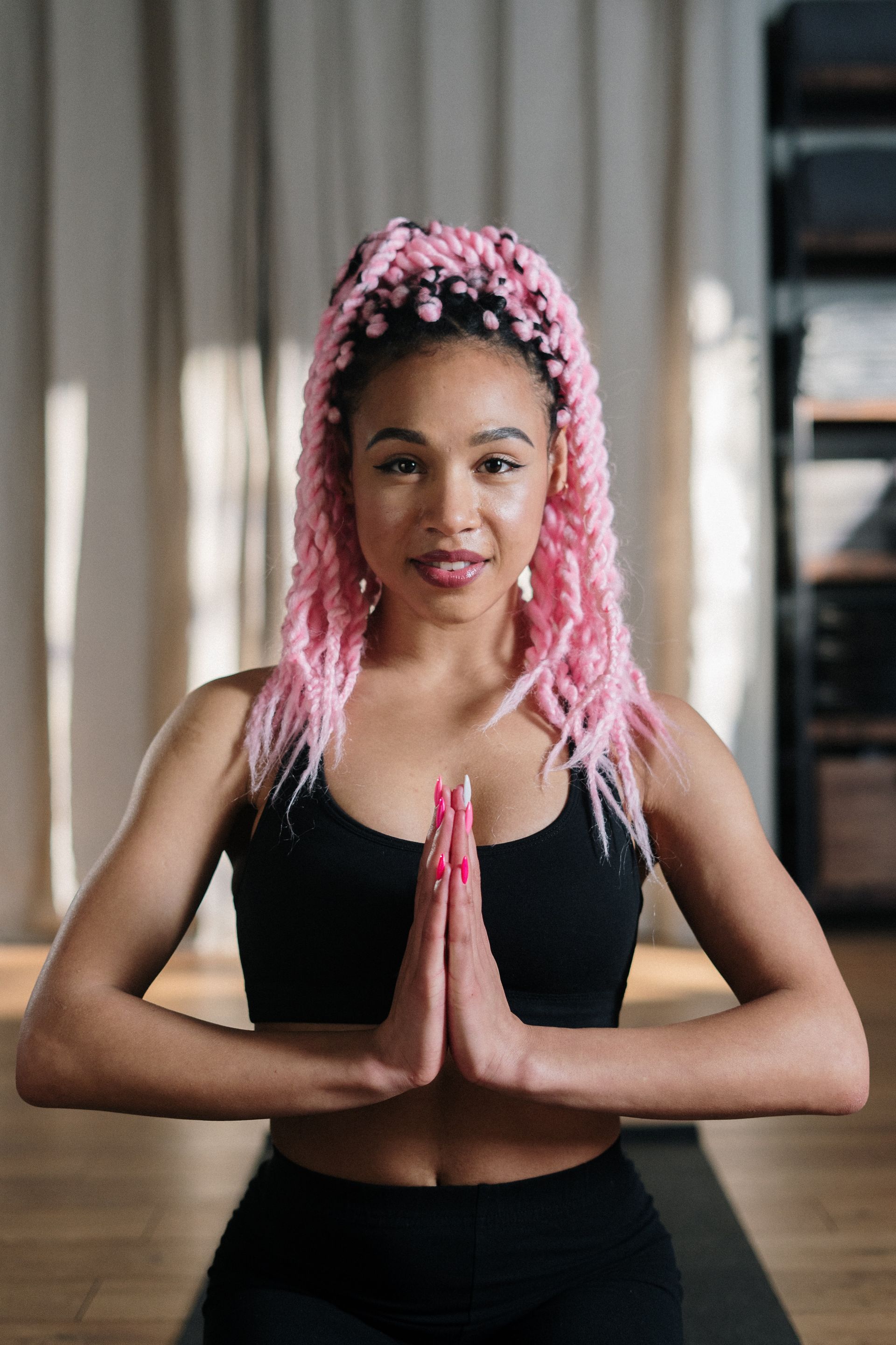 Woman with pink braids in yoga pose, hands together, wearing black sports bra.