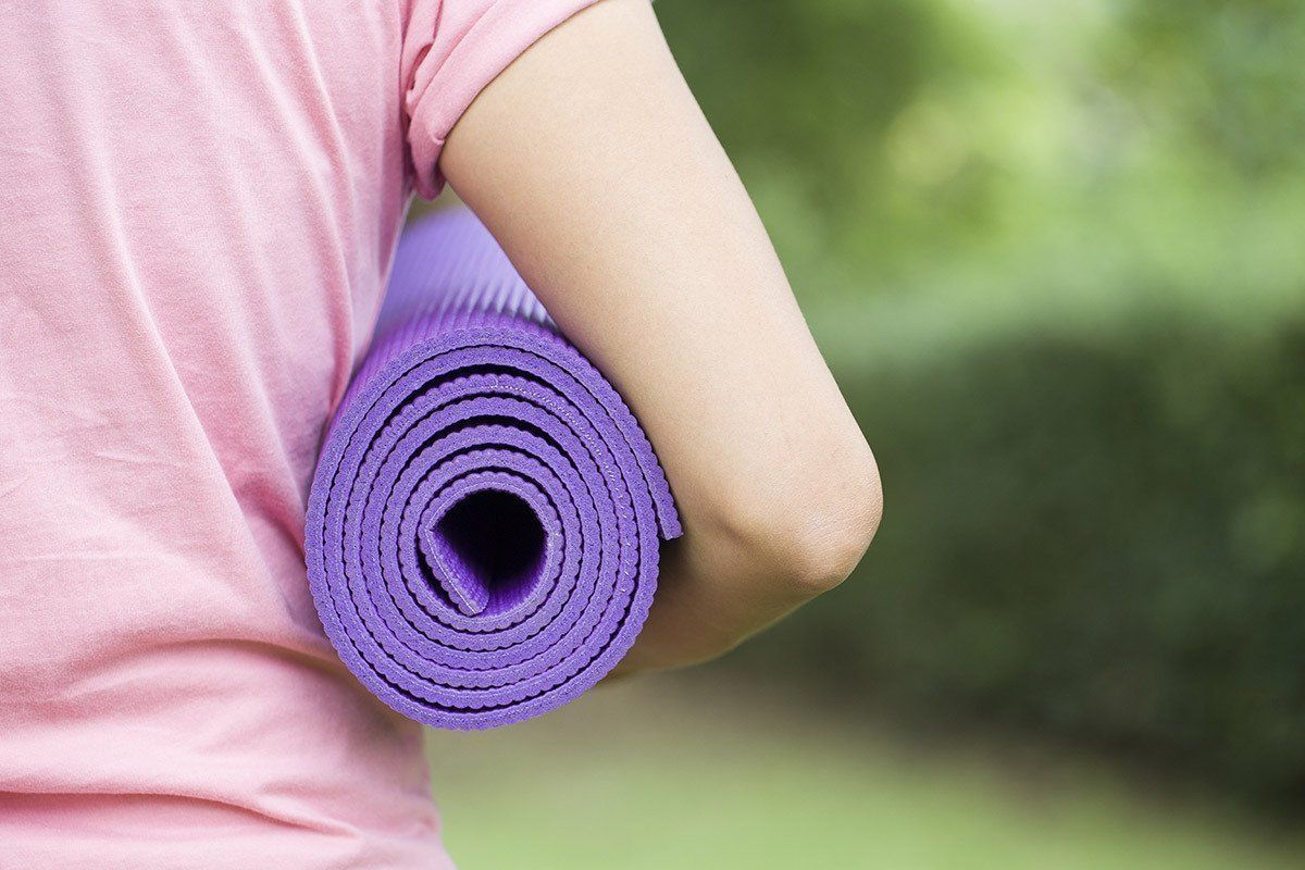 A woman in a pink shirt is holding a purple yoga mat