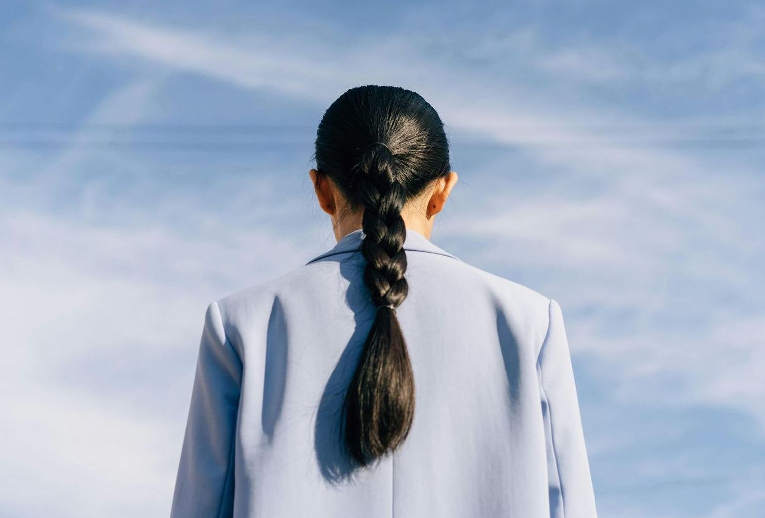 A woman with long hair in a ponytail is standing in front of a blue sky.