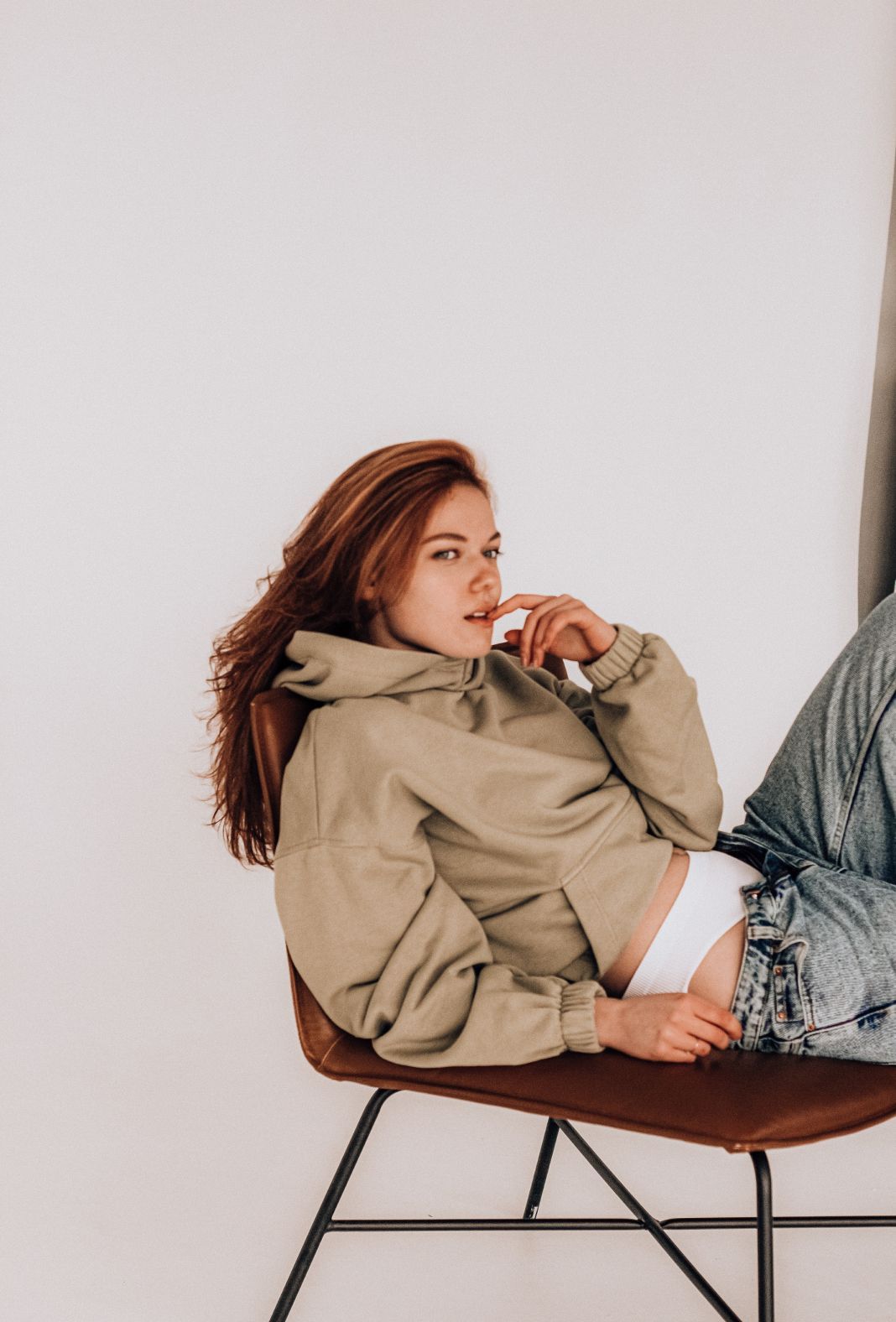 A woman is sitting on a chair wearing a hoodie and jeans.