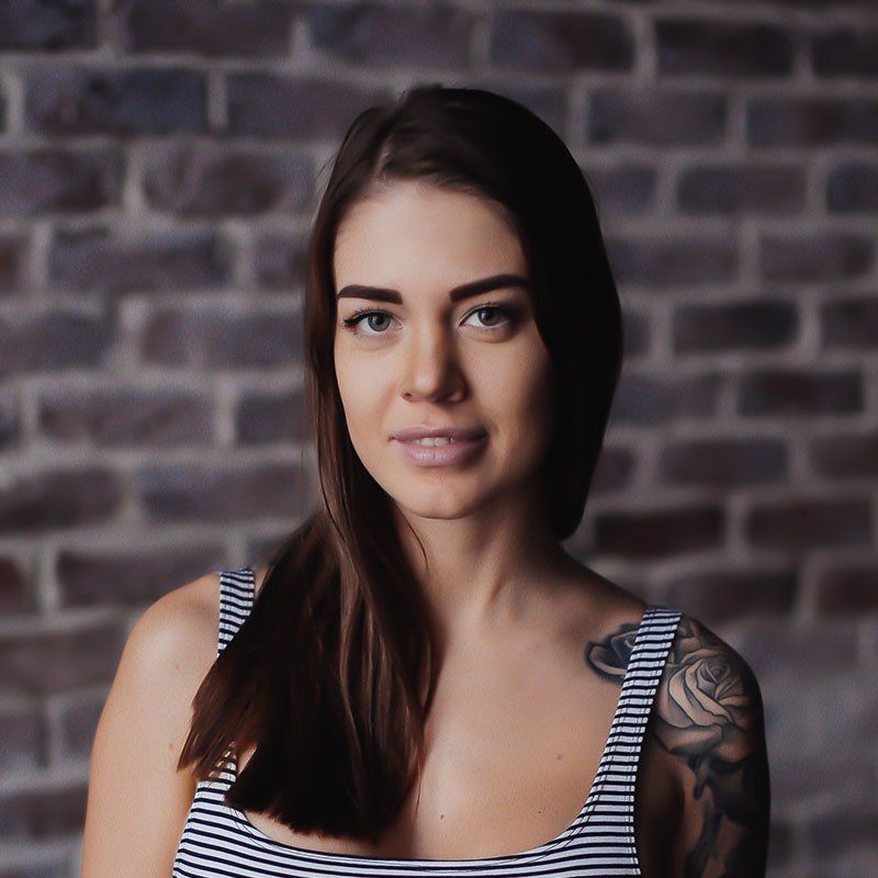 a woman with a tattoo on her arm stands in front of a brick wall