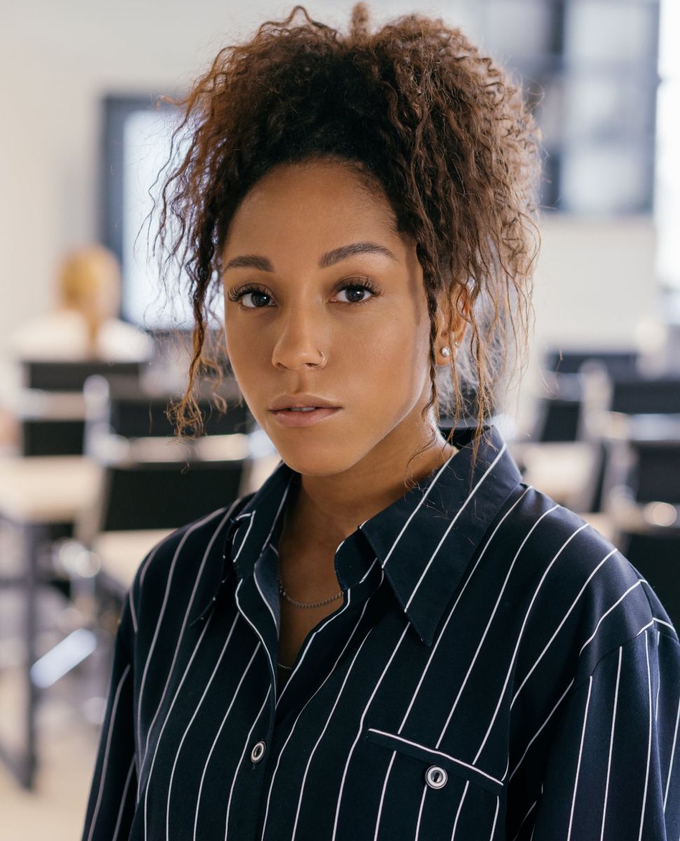 A woman with curly hair is wearing a striped shirt and looking at the camera.