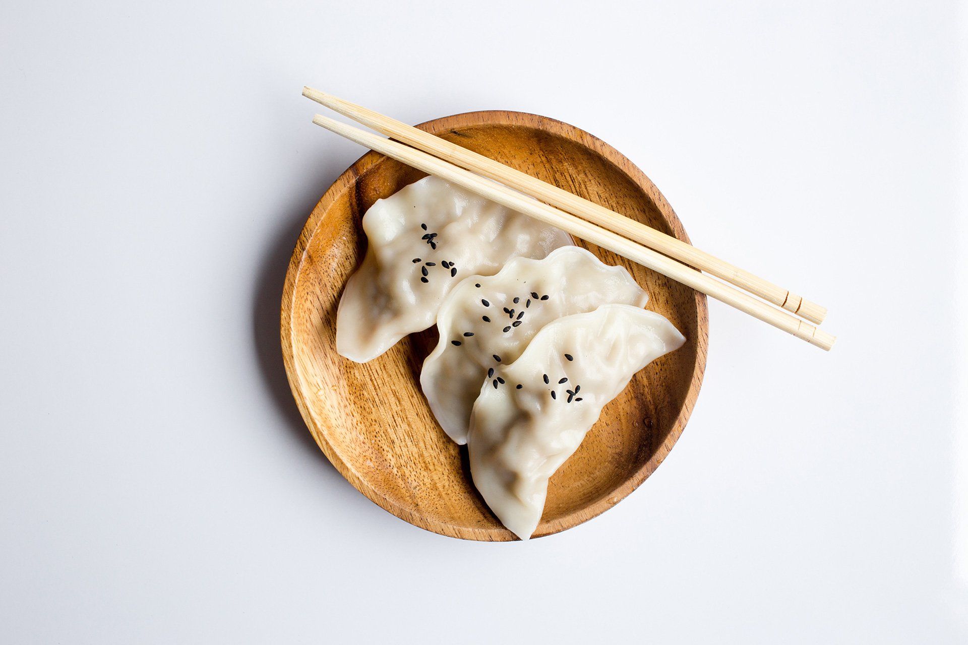 A wooden plate topped with dumplings and chopsticks.