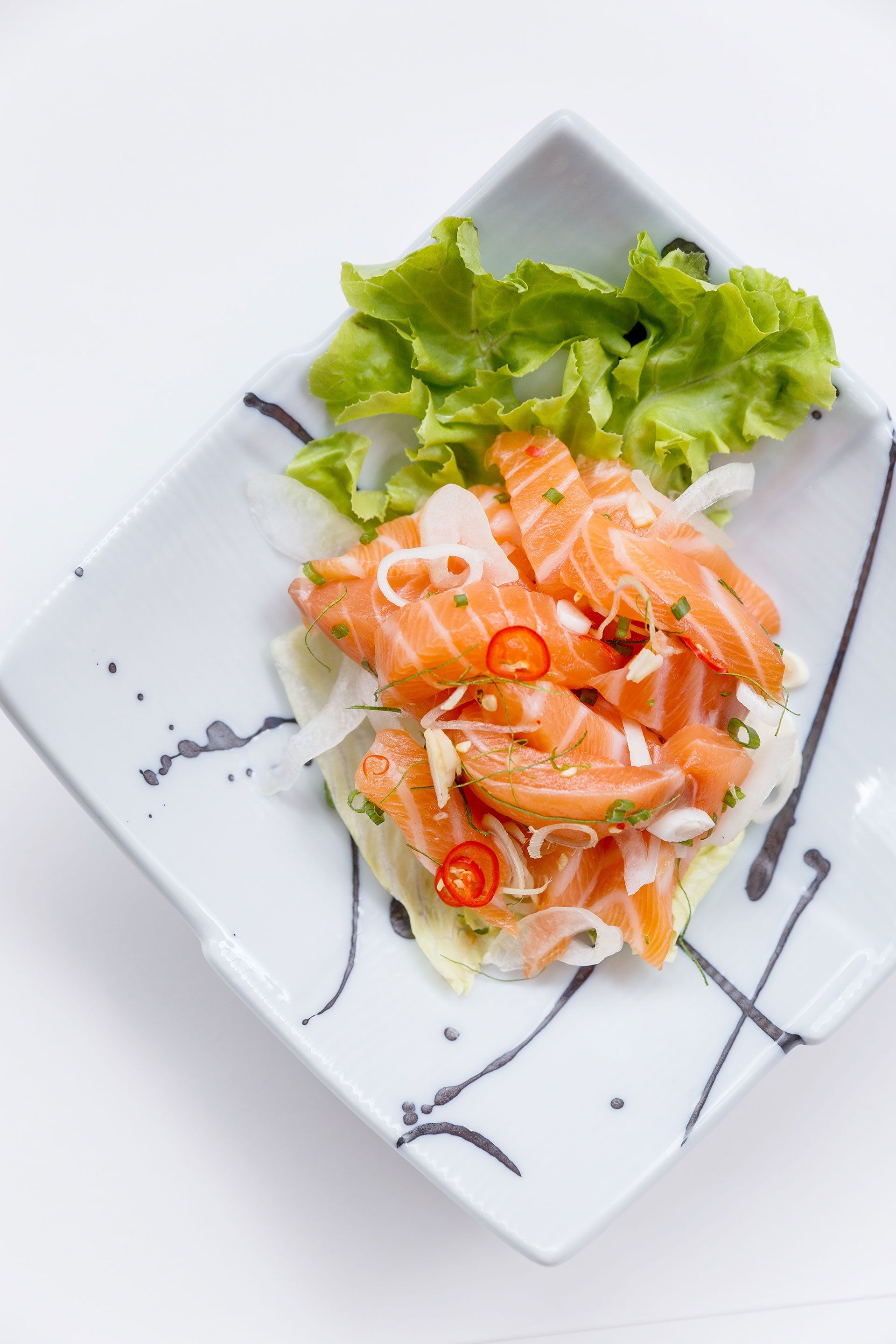 A white plate topped with salmon and lettuce on a table.
